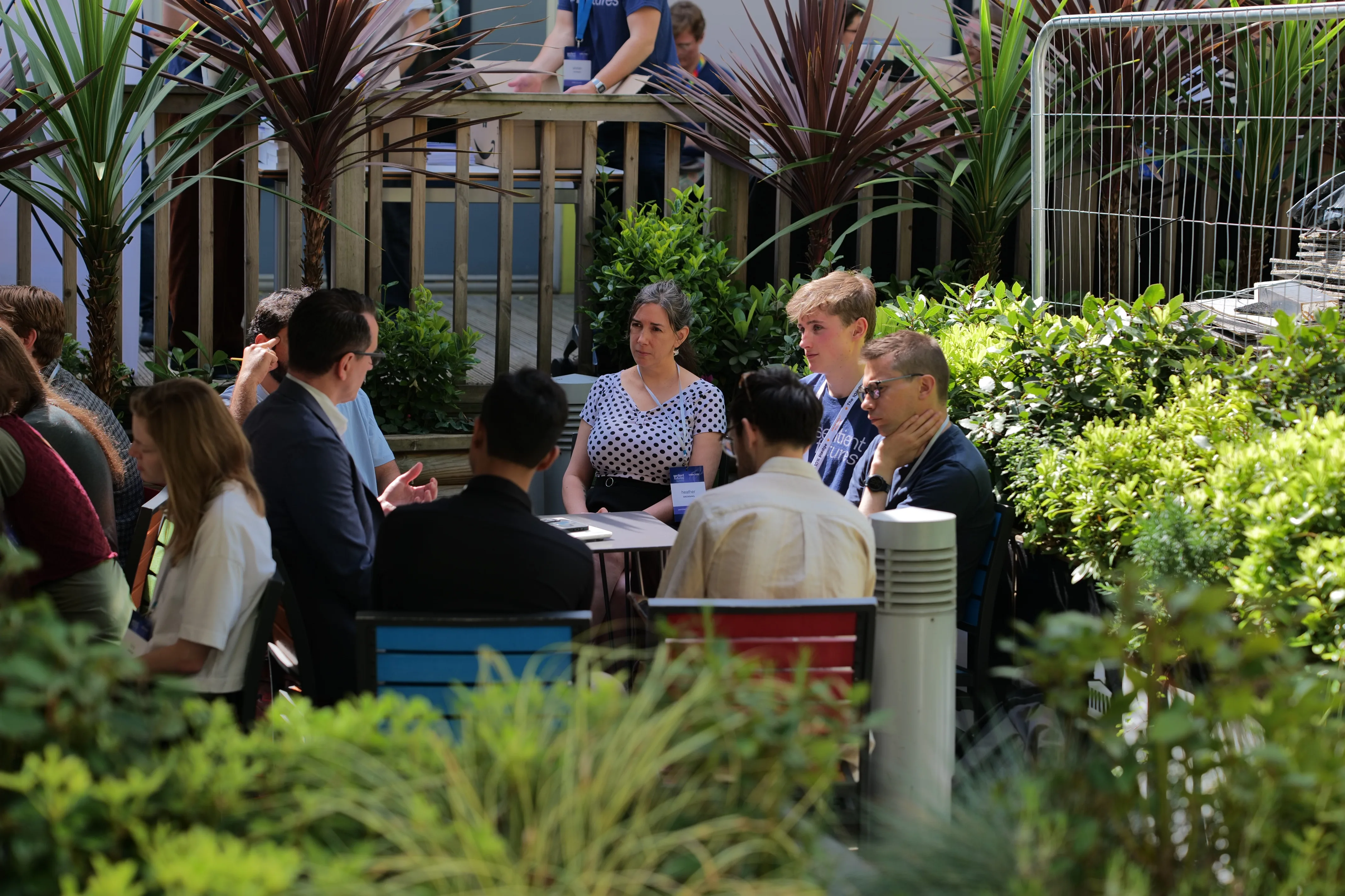 a table of attendees talking in a planted courtyard, sun through the leaves